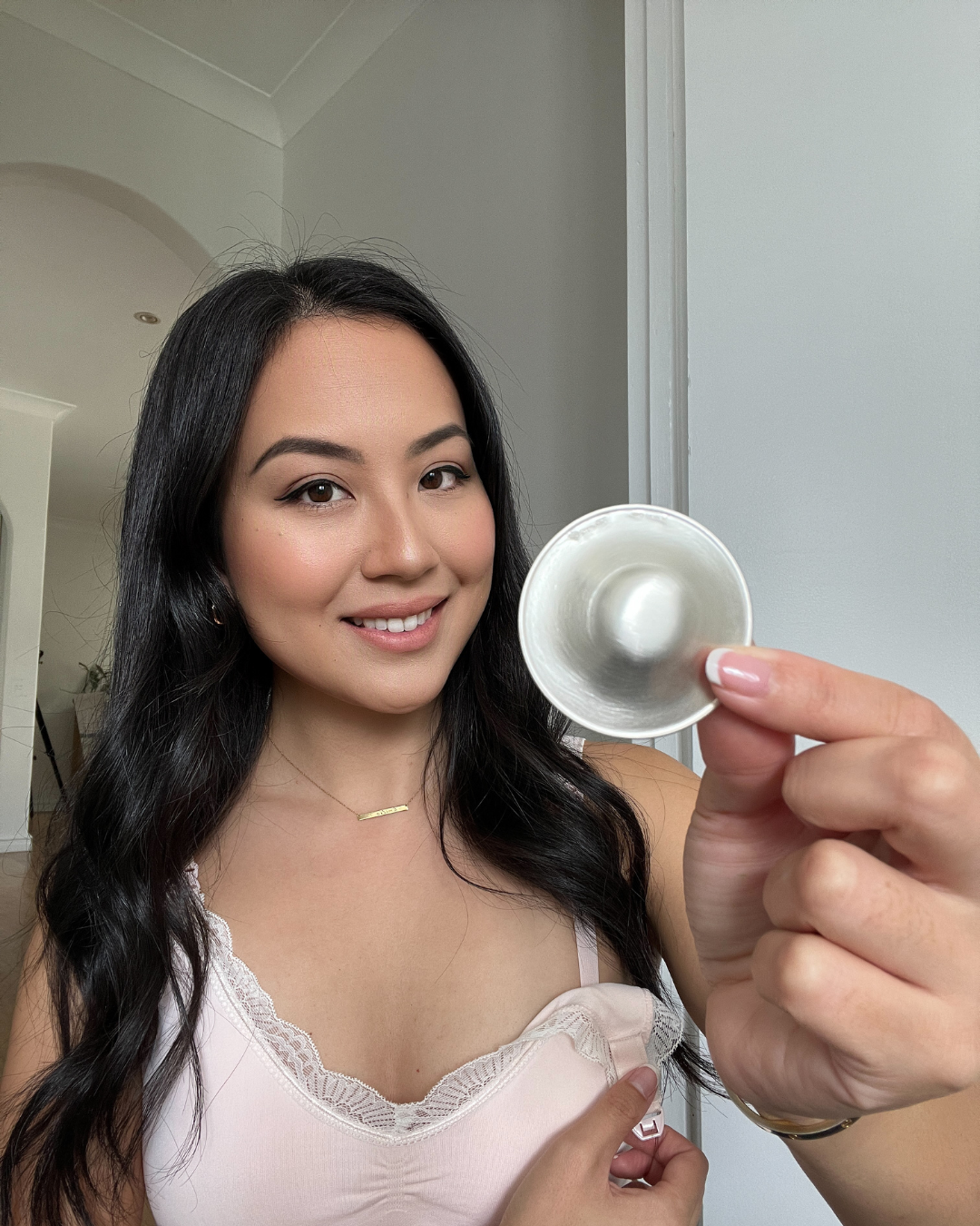 Smiling mum in a nursing bra holding up a Silverette silver nursing cup with its clear O-Feel silicone ring