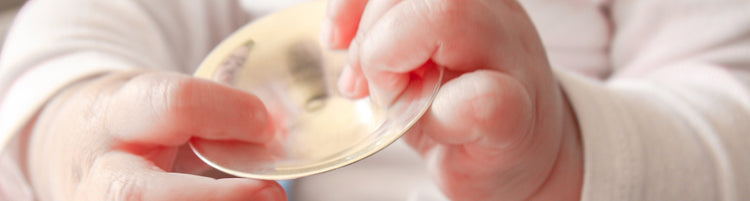 Baby's tiny hand and mum's hand holding a Silverette silver nursing cup